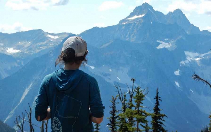 a person wearing a hat looks out over a mountainous landscape